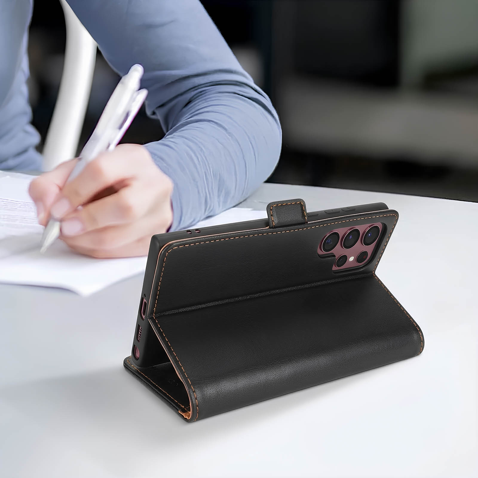 Una persona scrive su carta, un telefono nero in custodia è accanto.