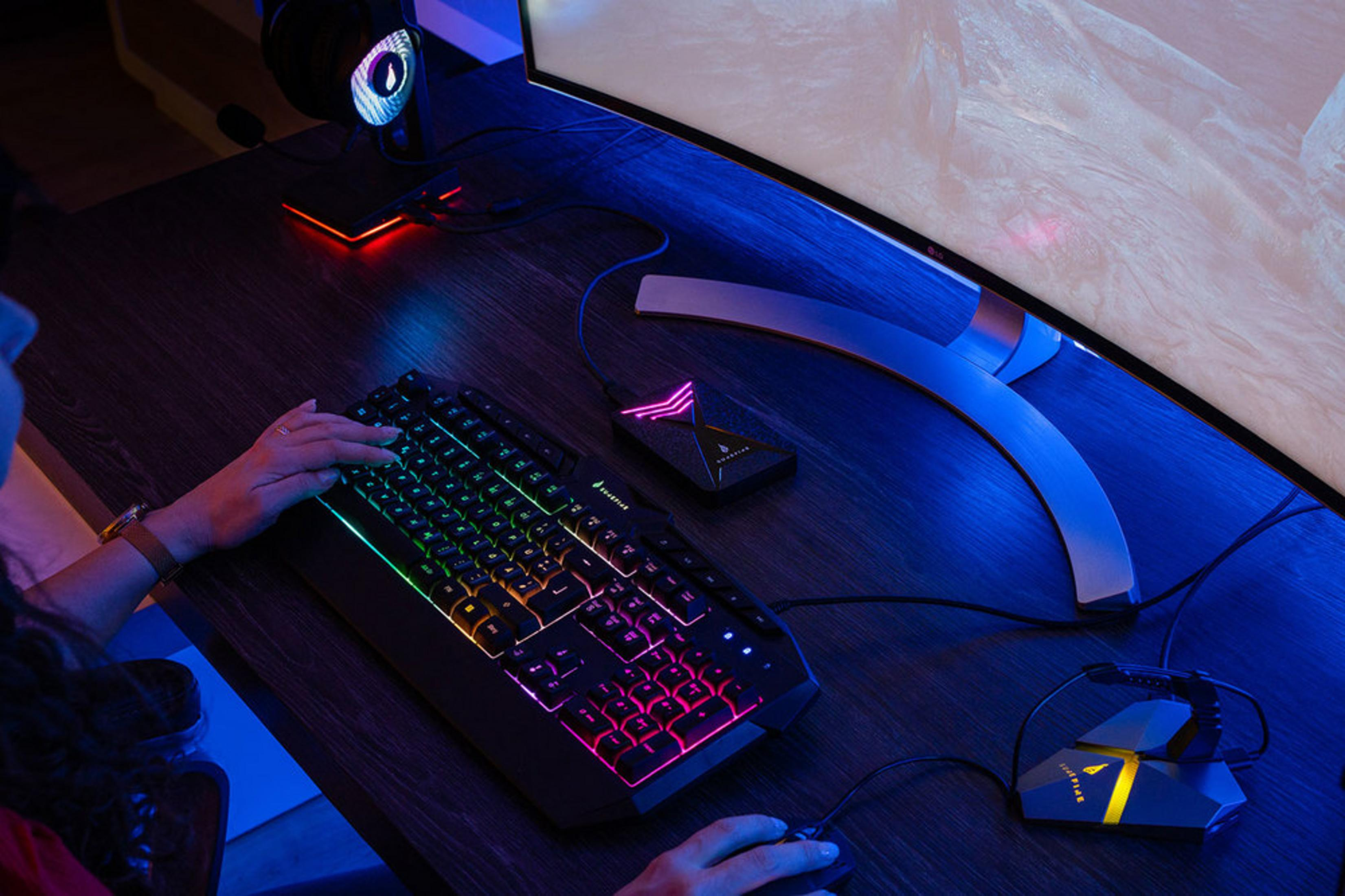 Osoba gra przy biurku z podświetlaną klawiaturą i myszką.