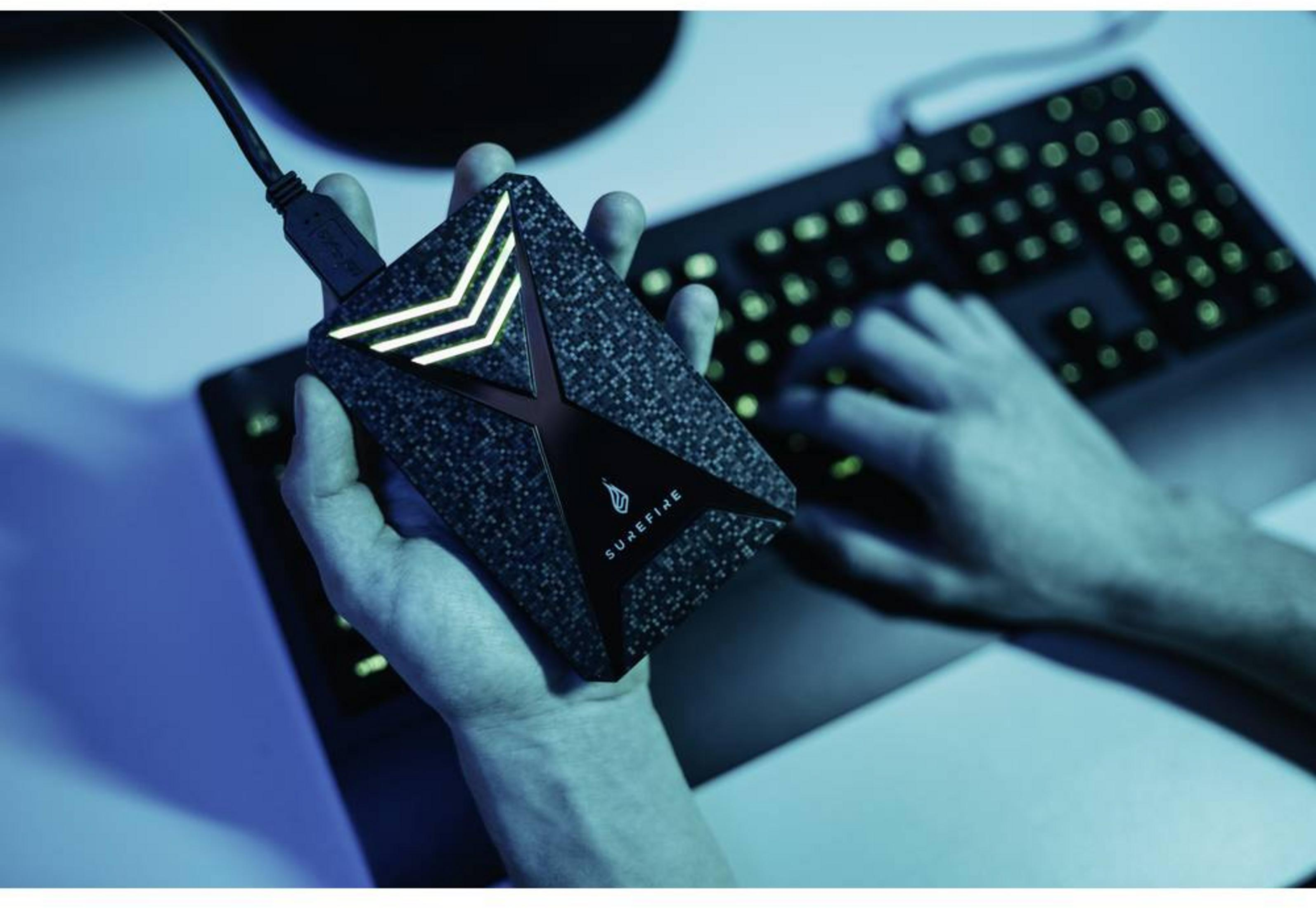 Ręka trzyma dysk zewnętrzny z podświetlanymi strzałkami przed klawiaturą.