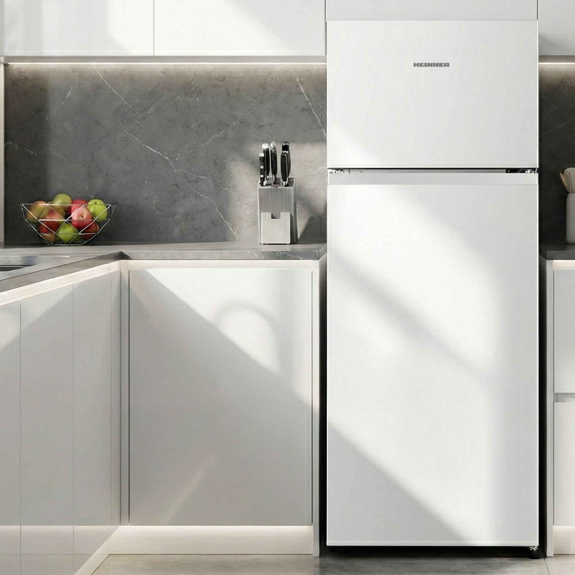 White kitchen counter with fruit basket, knife block and HEINNER fridge.