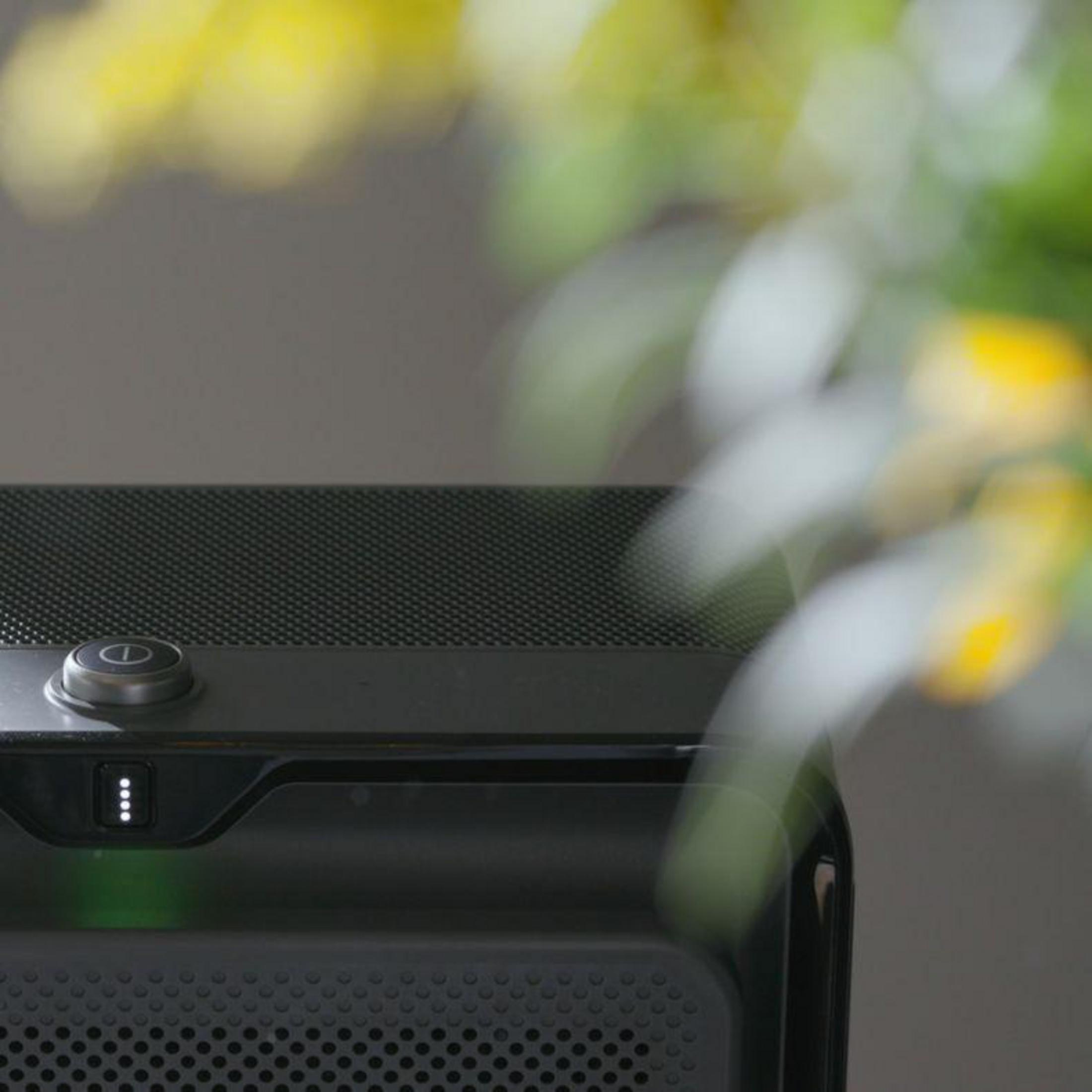 Un dispositivo nero con un pulsante e quattro luci, con fiori sfocati in primo piano.