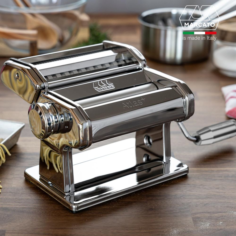 Eine glänzende Chrom-Nudelmaschine steht auf einem Holztisch. Mit Griff.