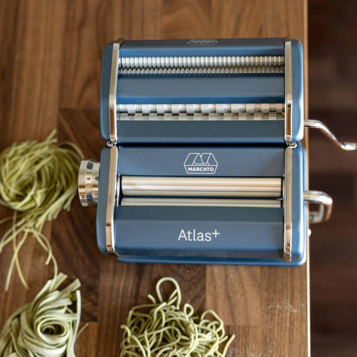 Blaue Marcato Atlas Nudelmaschine mit grünem Teig auf Holztisch.