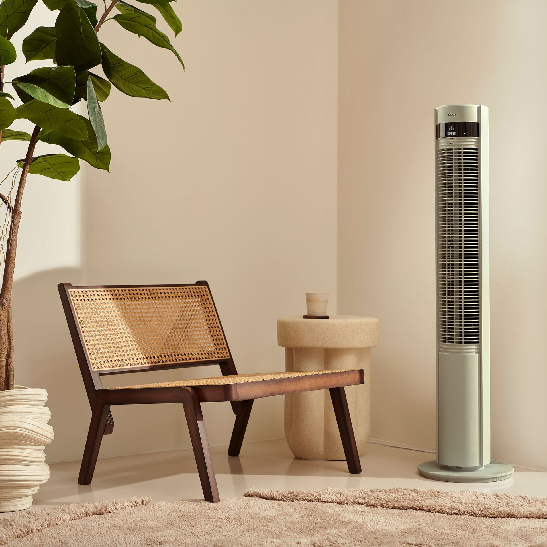 Een lichte kamer met rotan stoel, bijzettafel en torenventilator.