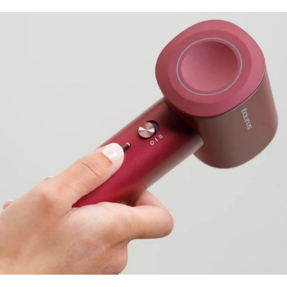 Dłoń trzyma czerwony suszarka do włosów z srebrnymi przyciskami. Widoczne logo 'Taurus'.