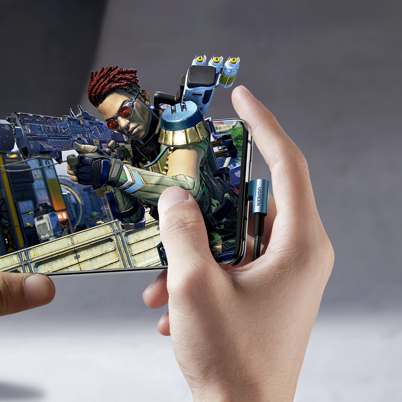 Una persona tiene uno smartphone con un gioco sparatutto. Un cavo di ricarica è collegato.