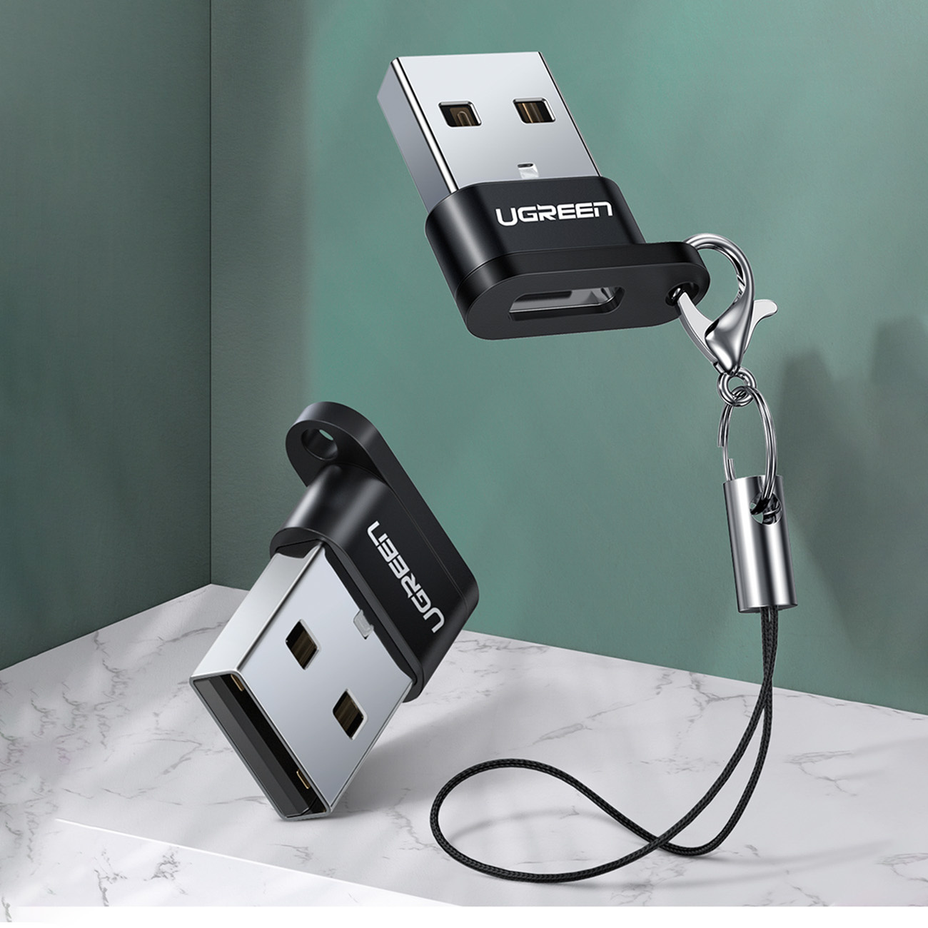 Mermer üzerinde iki UGREEN USB bellek, biri kordonlu, yeşil arka plan önünde.