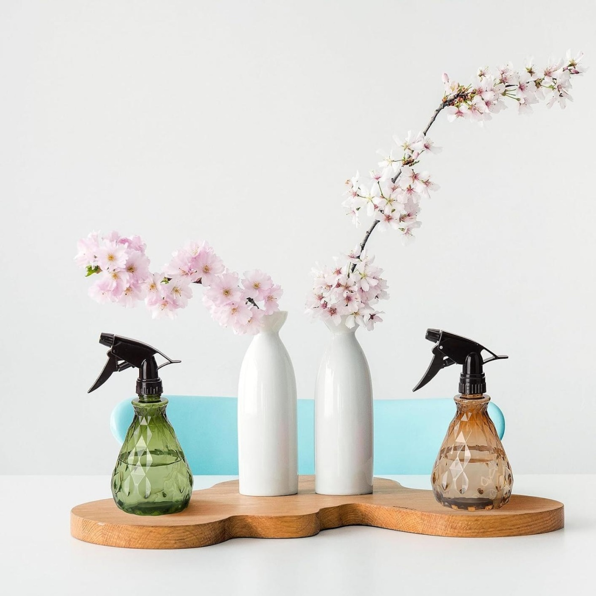 Zwei Sprühflaschen und zwei weiße Vasen mit Kirschblüten auf einem Holztablett.