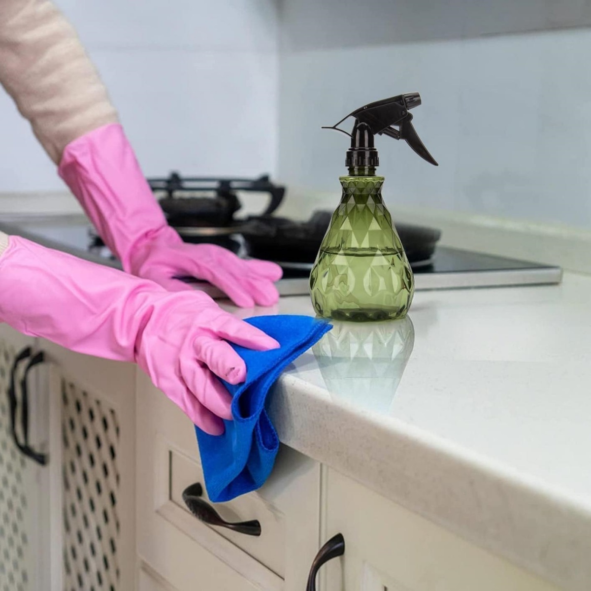 Person in rosa Handschuhen reinigt Küchentheke mit blauem Tuch.