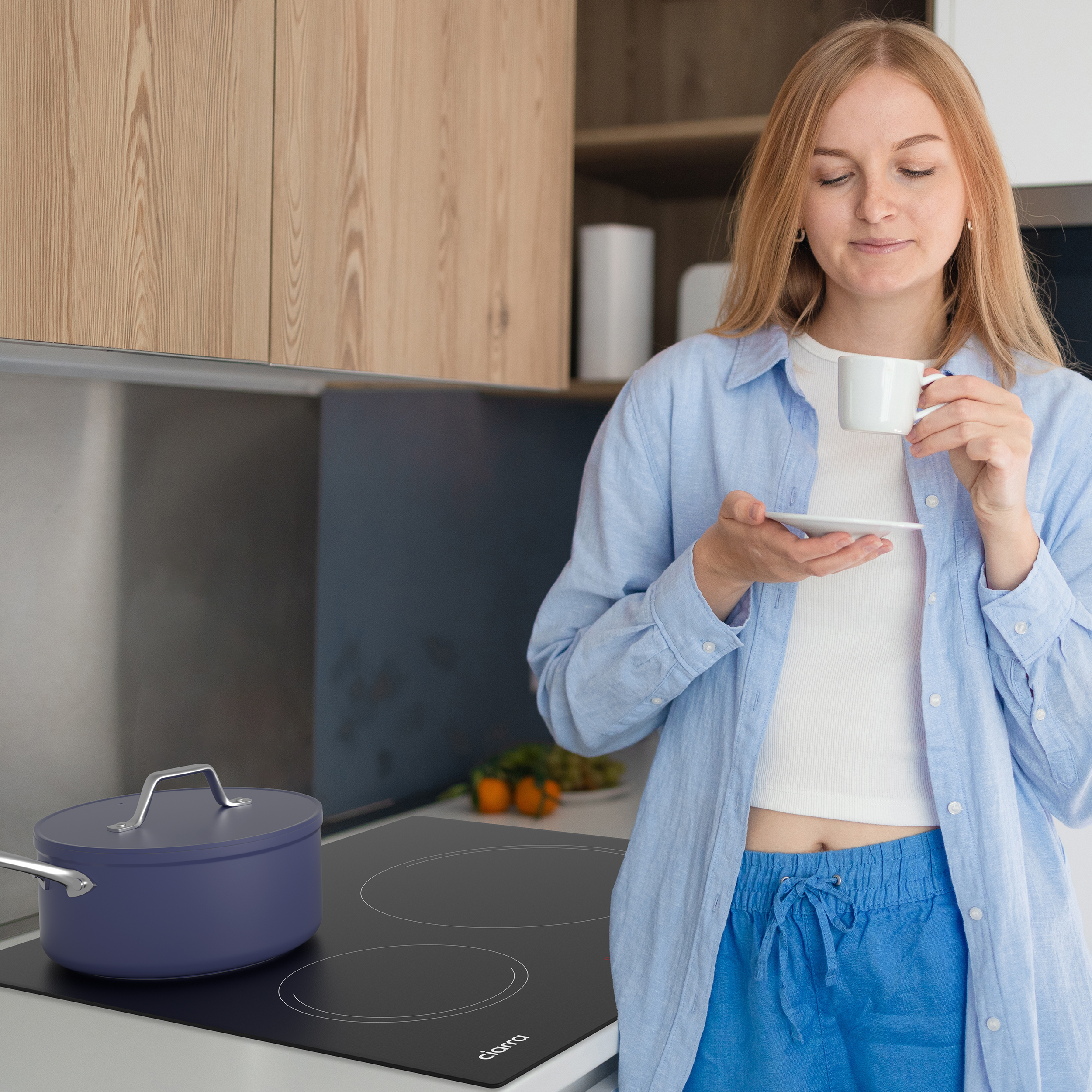 Eine Frau trinkt Kaffee in einer modernen Küche mit Kochtopf und Herd.