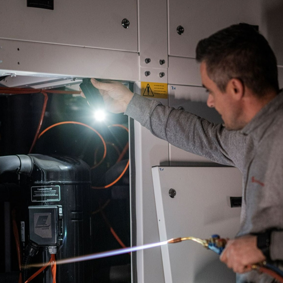 Un homme éclaire une machine avec une lampe de poche tout en travaillant avec un chalumeau.