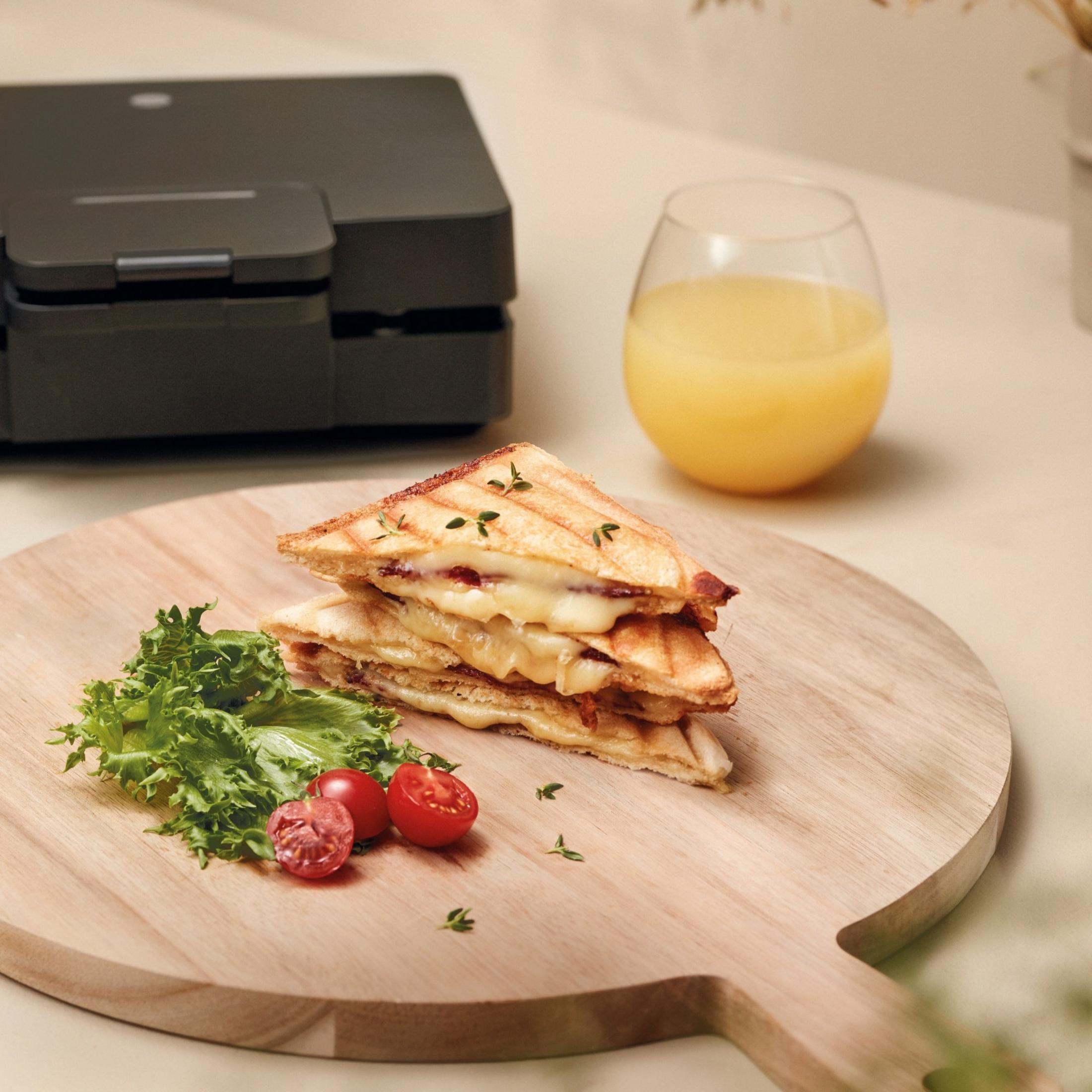 Gestapelte Sandwiches mit Käse, Beilagen und Saft auf Holzbrett.