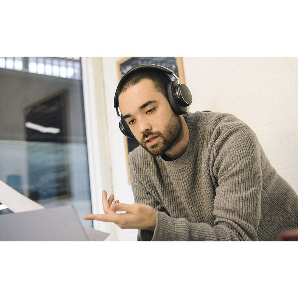 Mężczyzna w słuchawkach pochyla się nad laptopem, rozmawia.