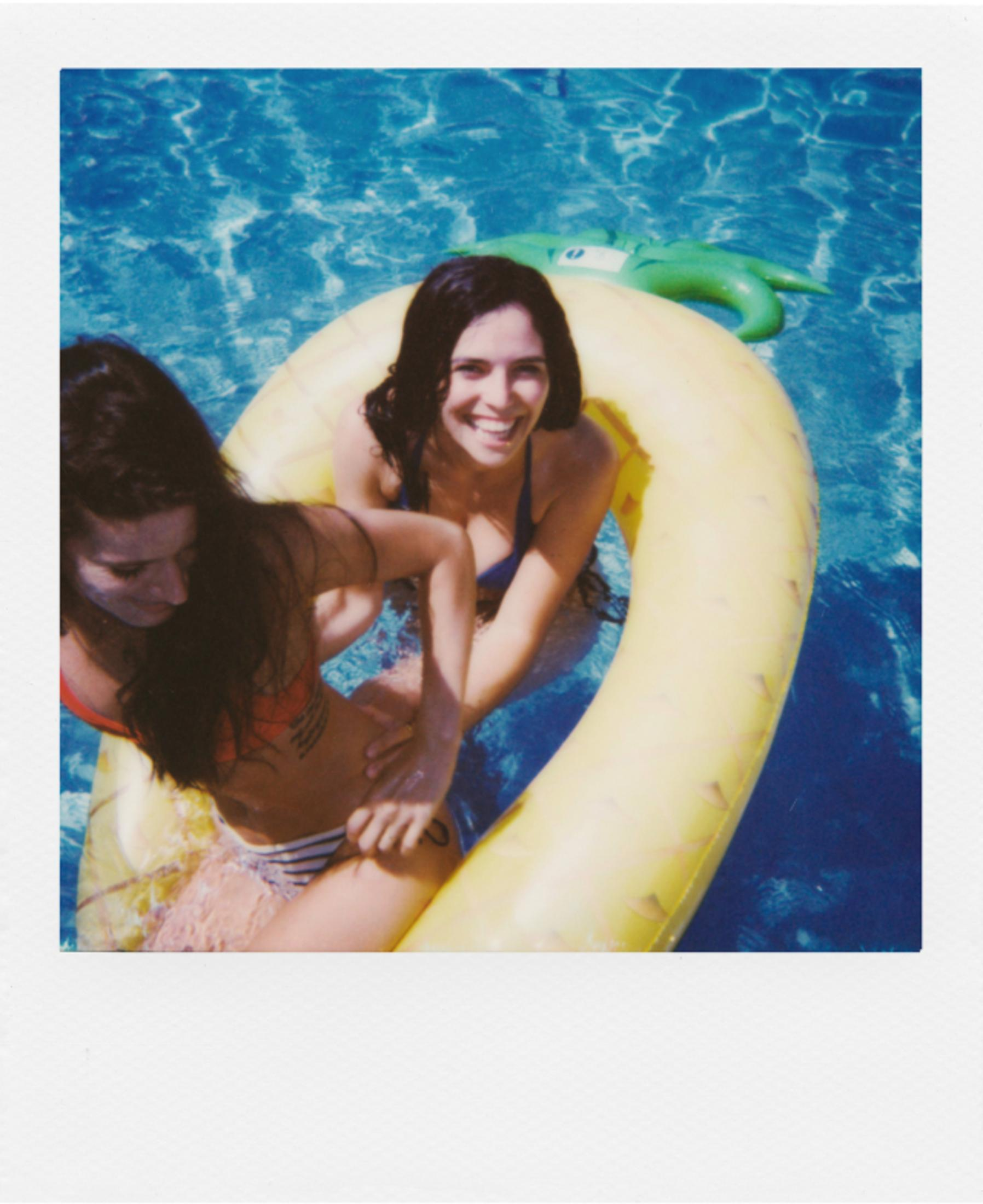 Dos mujeres en el agua sobre un flotador amarillo. Una sonríe.