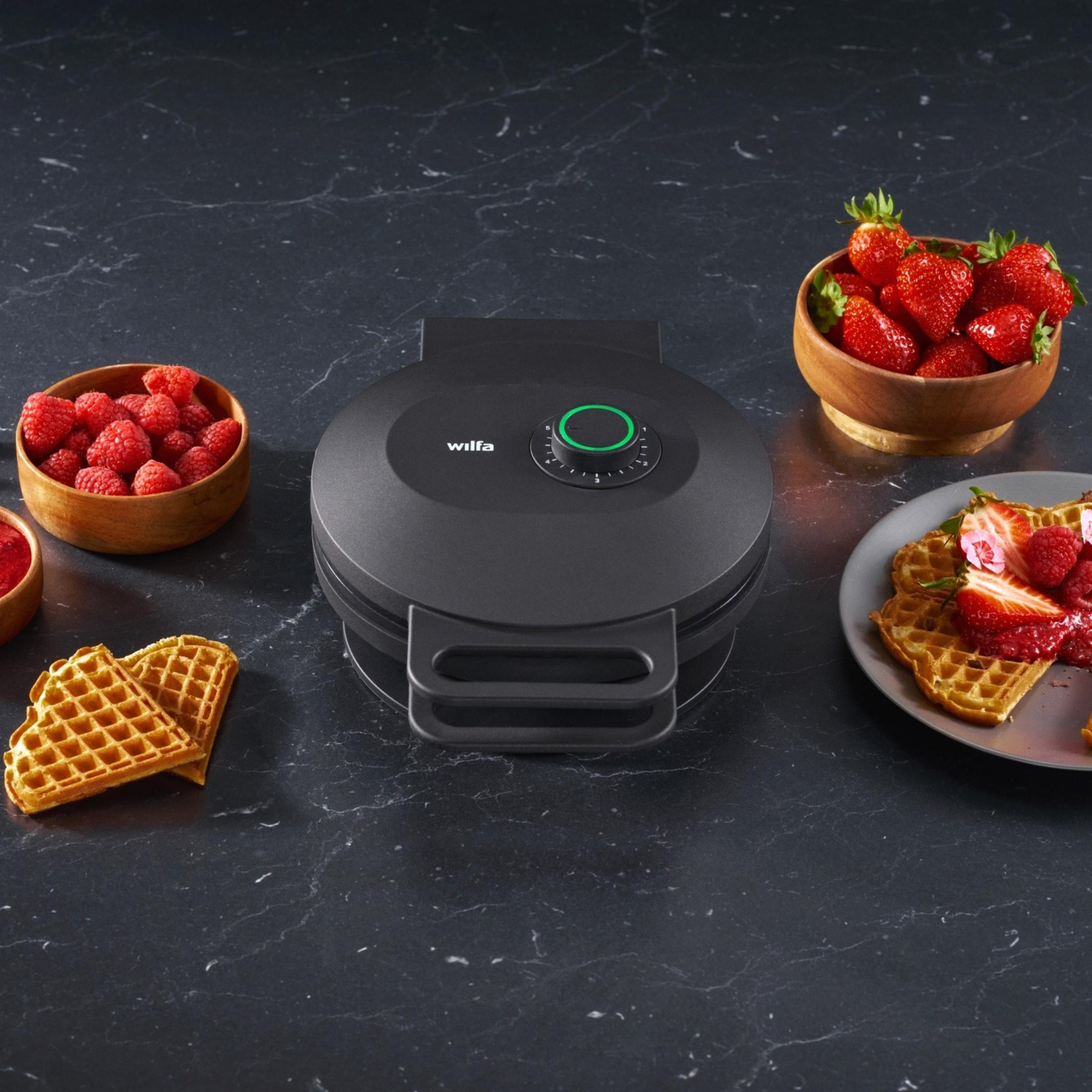 Ein Wilfa Waffeleisen mit Beeren und Waffeln auf dunklem Marmortisch.
