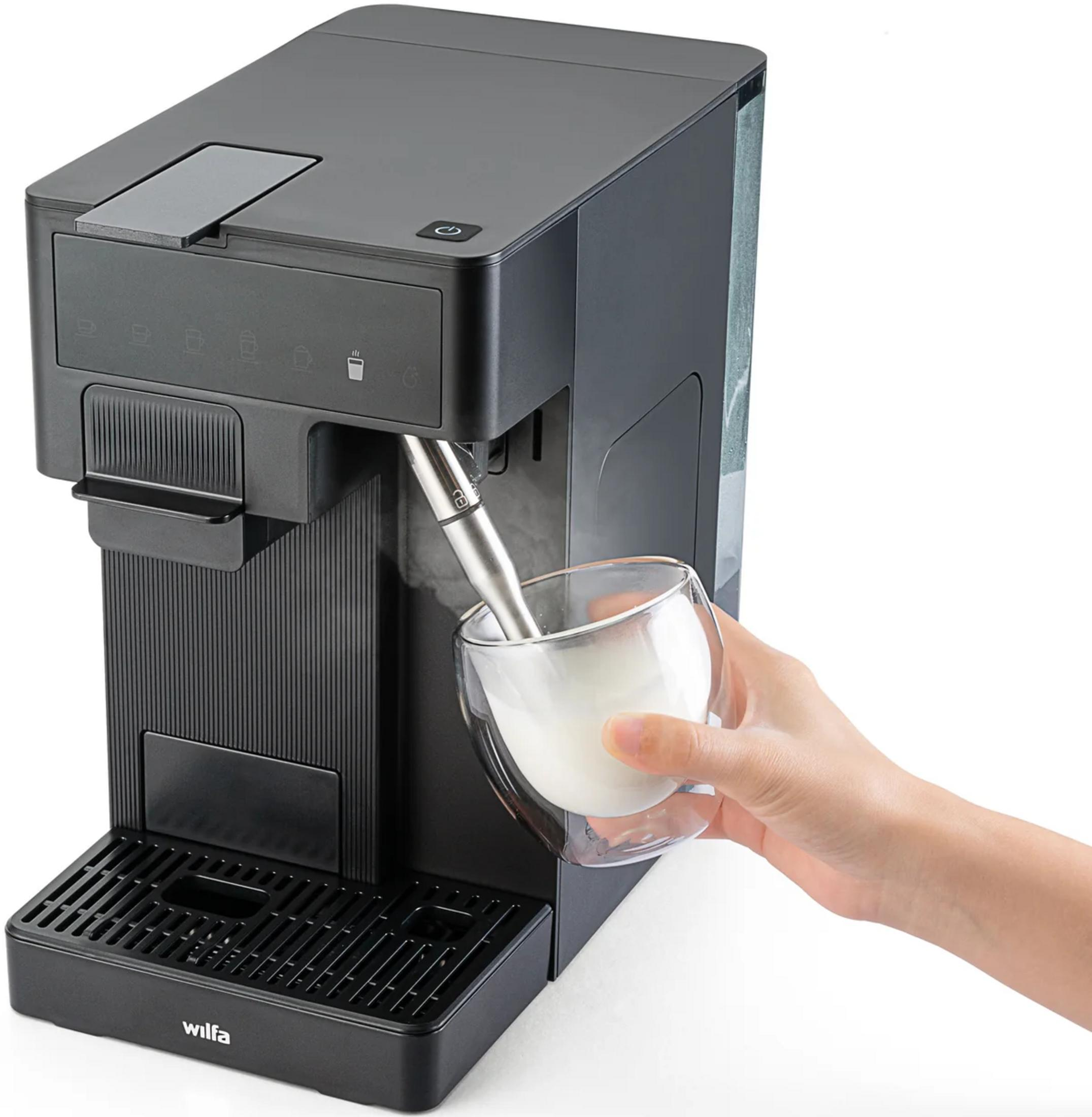 Una mano sostiene una taza de vidrio de doble pared bajo la lanza de vapor metálica de una cafetera.