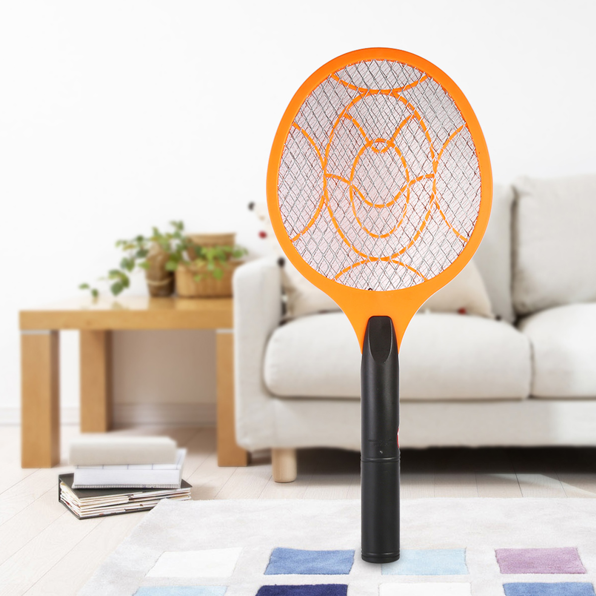 Eine orange elektrische Mückenklatsche steht in einem Wohnzimmer, nahe Büchern und einer Couch.