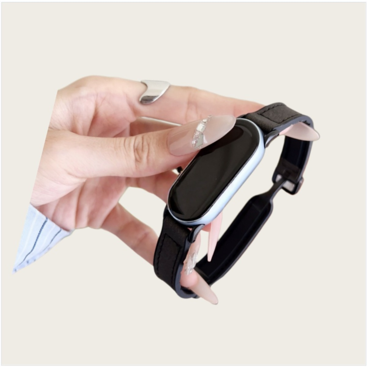 Eine Hand mit Maniküre hält eine schwarze Smartwatch mit silbernem Rand.