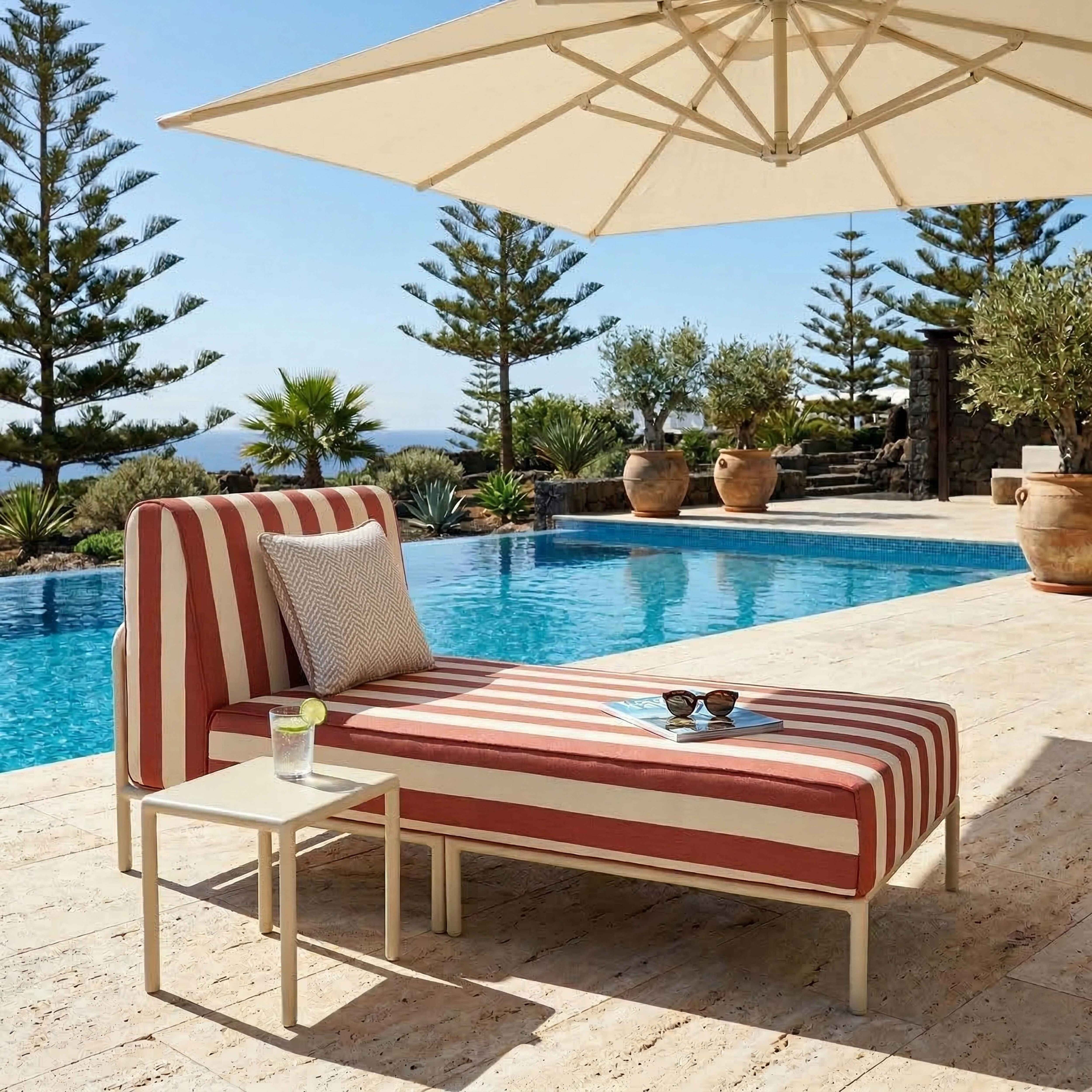 Eine gestreifte Liege am Pool unter einem Sonnenschirm mit Glas und Büchern.