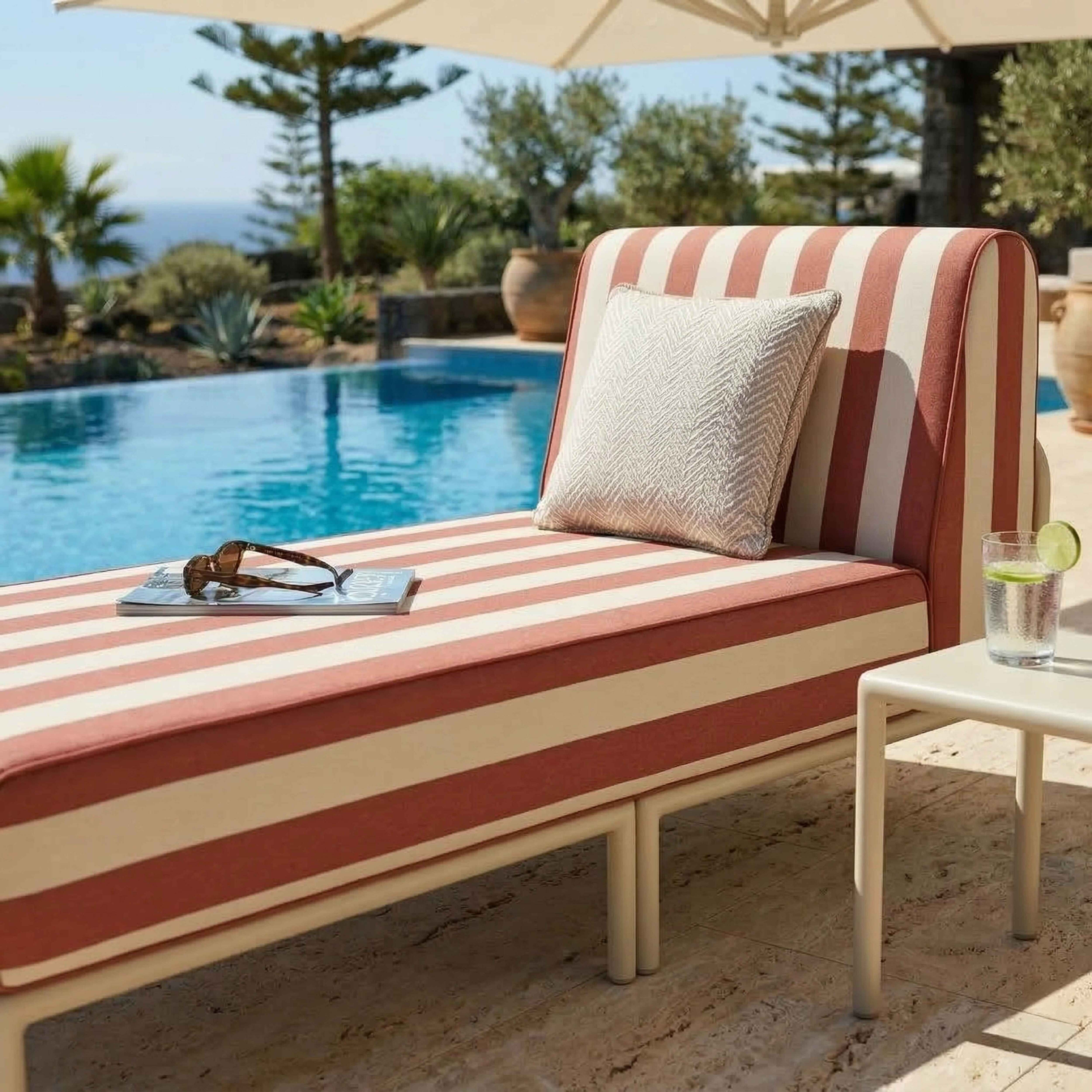 Eine gestreifte Liege am Pool mit einem Getränk und einer Brille.