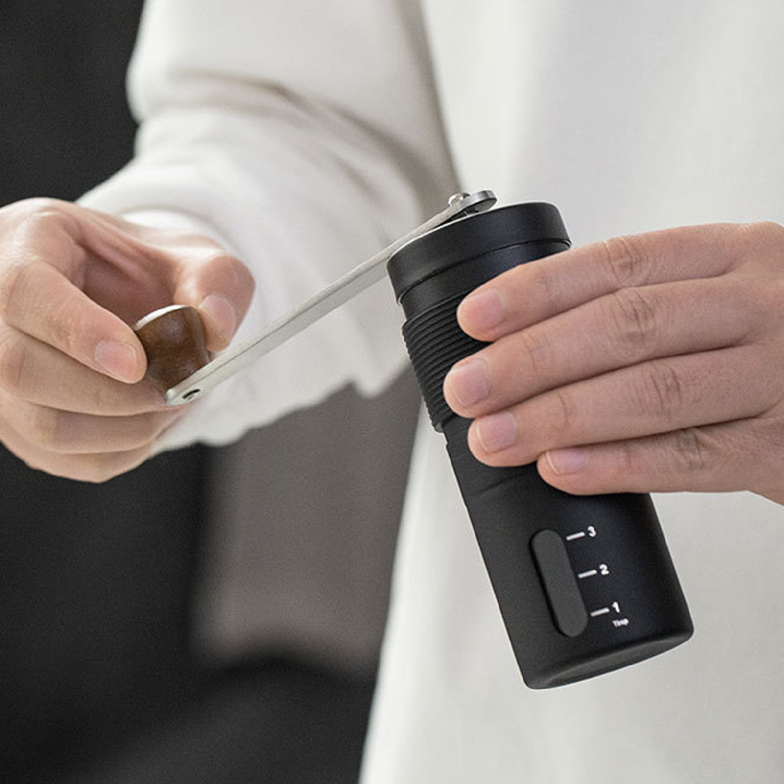 Eine Person dreht mit der Hand an einer schwarzen Kaffeemühle mit Metallschaft.