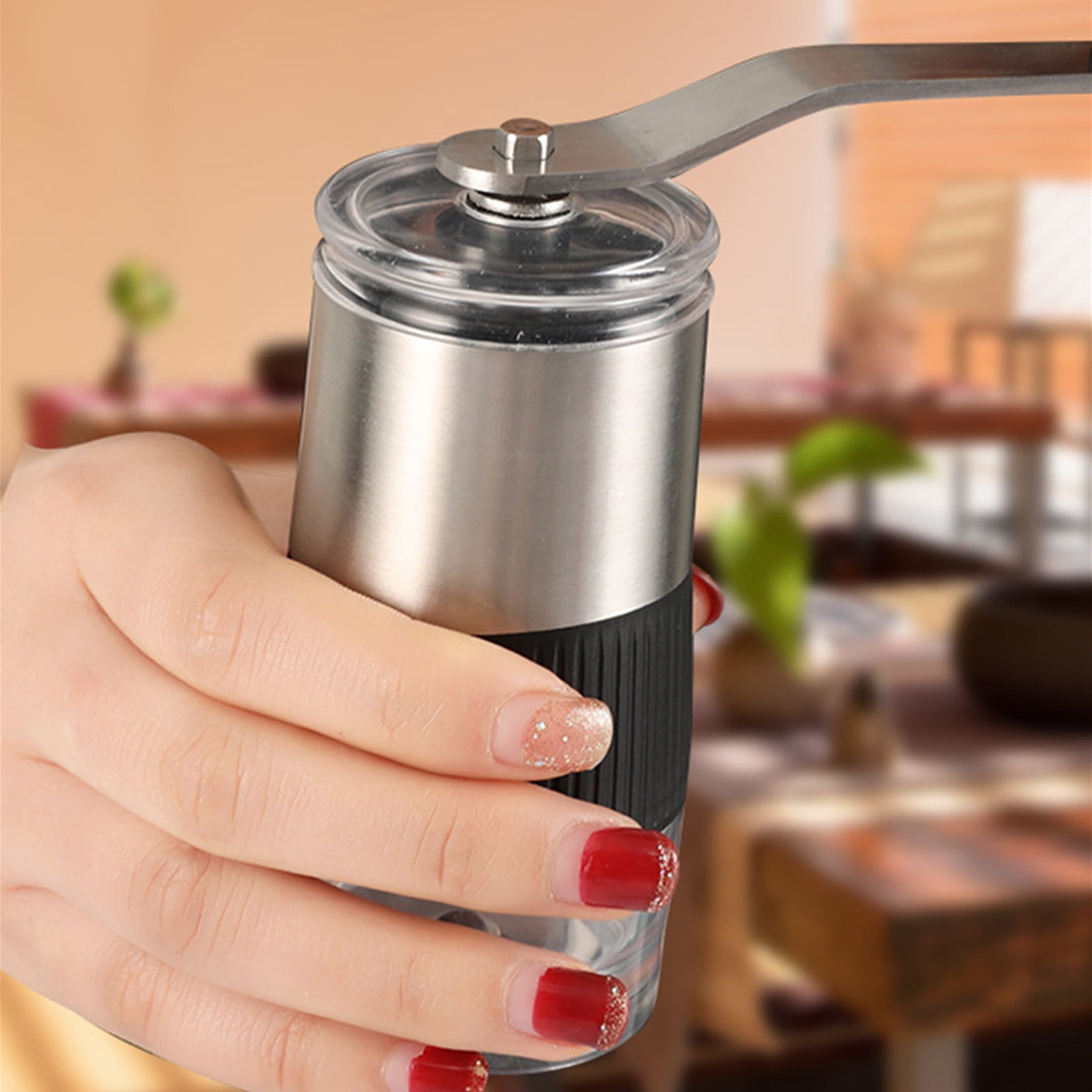 Eine Hand hält eine silberne Kaffeemühle mit Kurbel. Hintergrund unscharf.