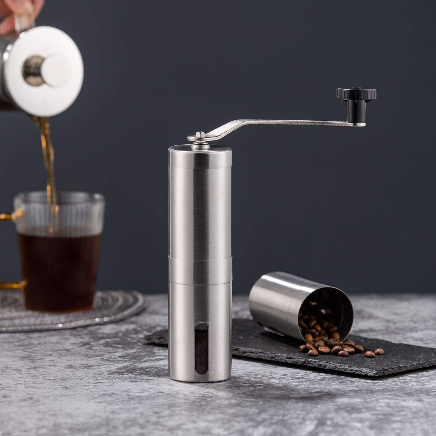 Eine Edelstahl-Kaffeemühle steht neben einer Tasse Kaffee und Kaffeebohnen.