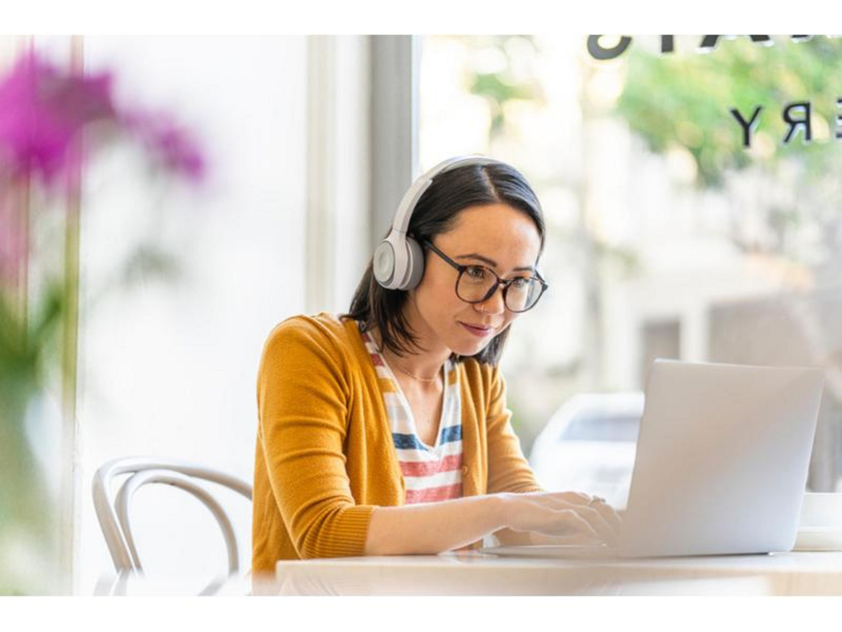 Kobieta w słuchawkach i okularach pracuje na laptopie na zewnątrz.