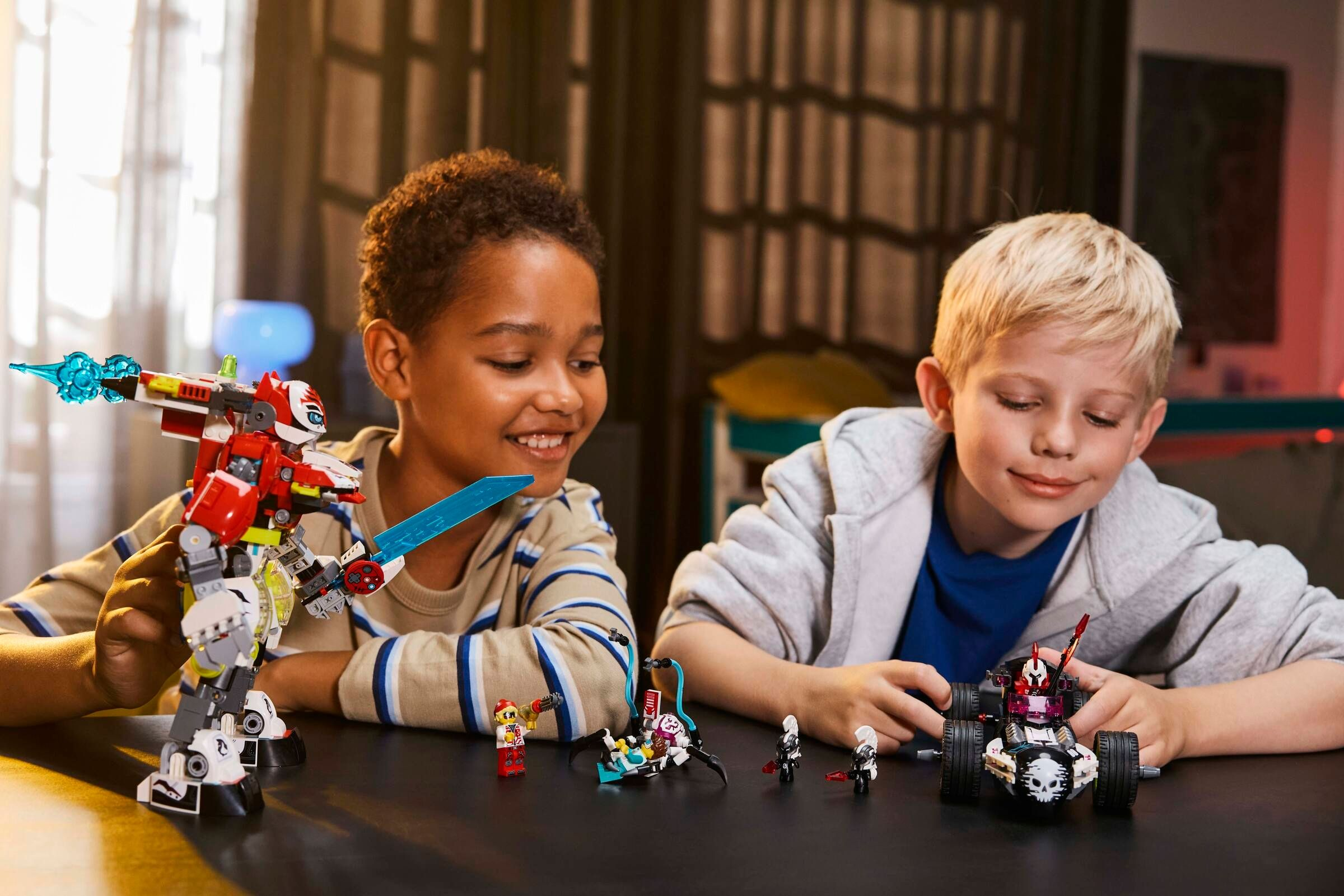 Zwei Jungen spielen mit Lego-Robotern und Fahrzeugen auf einem Tisch.