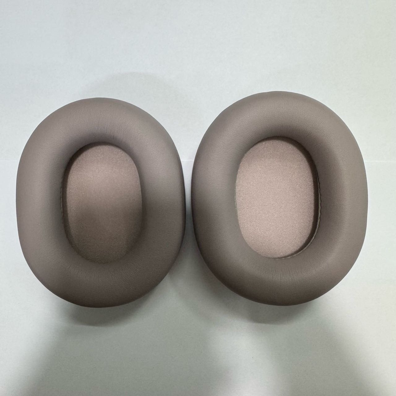Due cuscinetti auricolari ovali beige sono uno accanto all'altro su sfondo bianco.