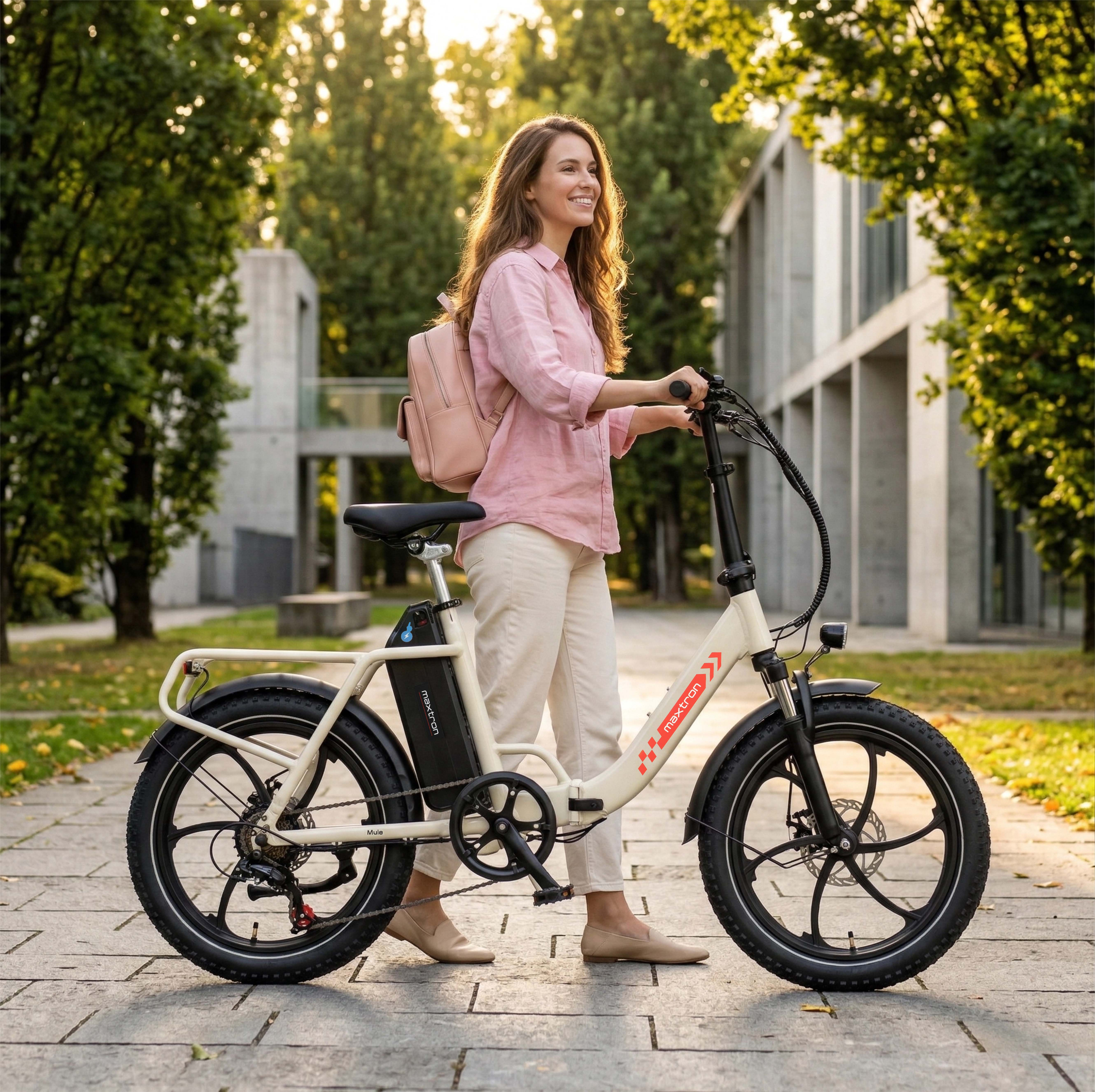 Frau mit rosa Hemd und Rucksack steht neben einem cremefarbenen E-Bike auf einem gepflasterten Weg.