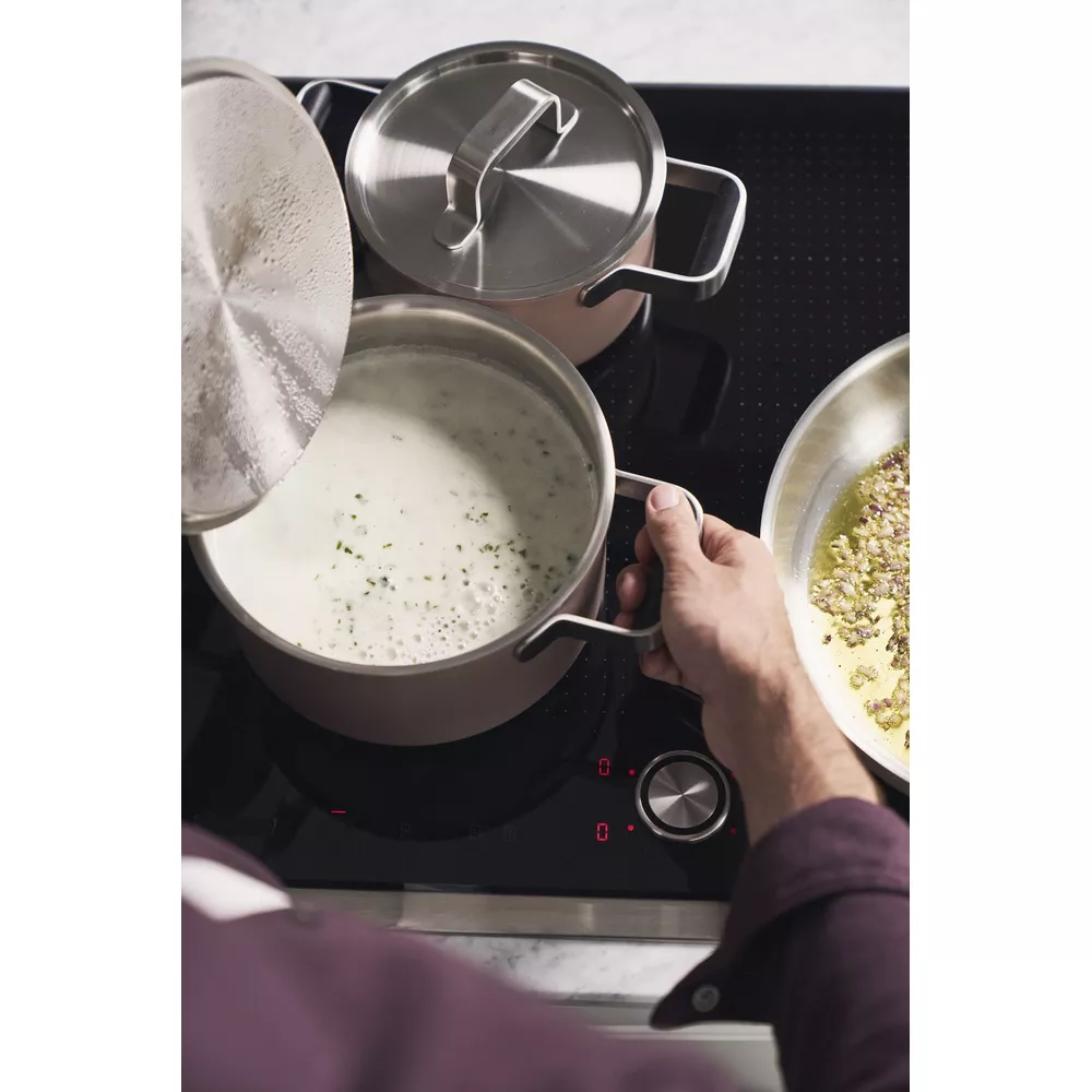 Una mano levanta la tapa de una olla con líquido blanco en una estufa.