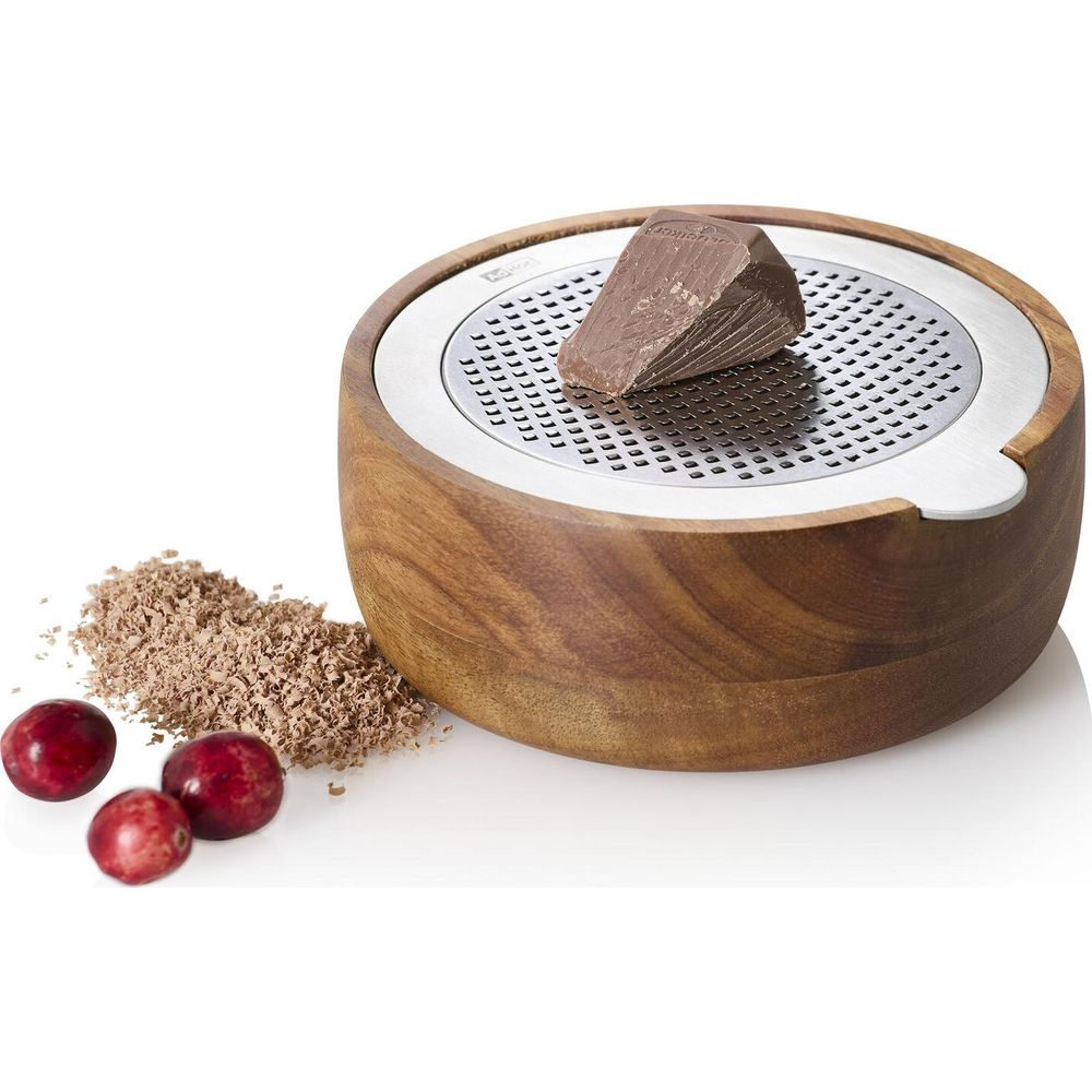 Un pezzo di cioccolato su una grattugia di legno con scaglie e bacche accanto.