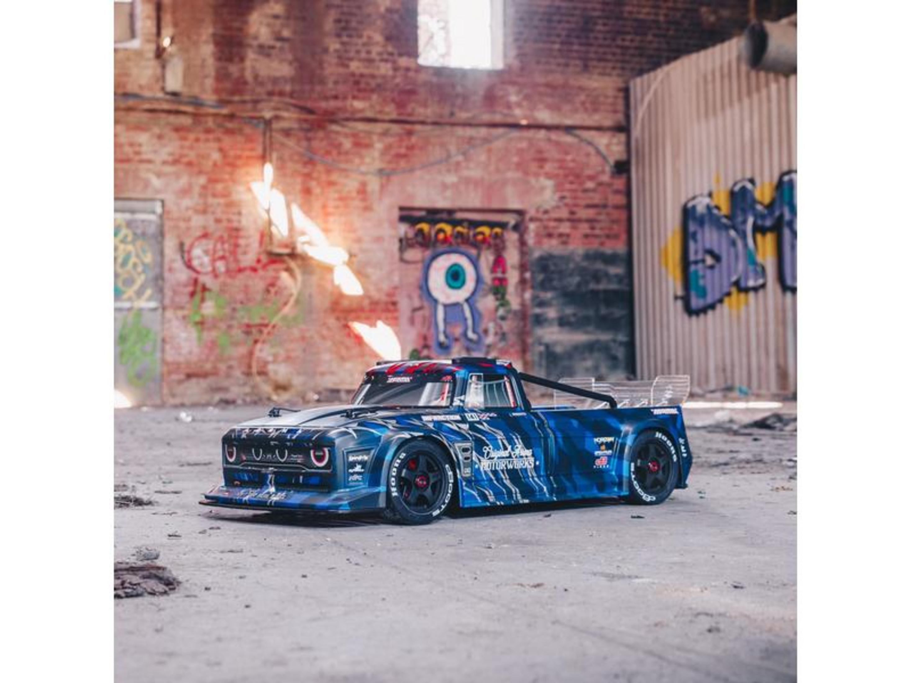 Une voiture de course RC bleue rayée de blanc se trouve dans un entrepôt abandonné tagué.