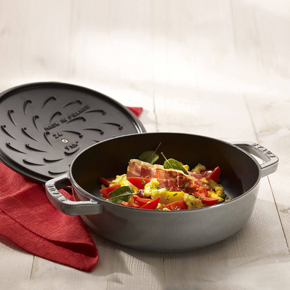 Grauer Topf mit Essen, Deckel daneben auf roter Serviette. Holzhintergrund.