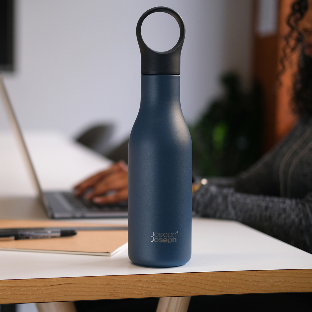Dunkelblaue Joseph Joseph Wasserflasche auf einem Schreibtisch mit Laptop und Notizbuch.