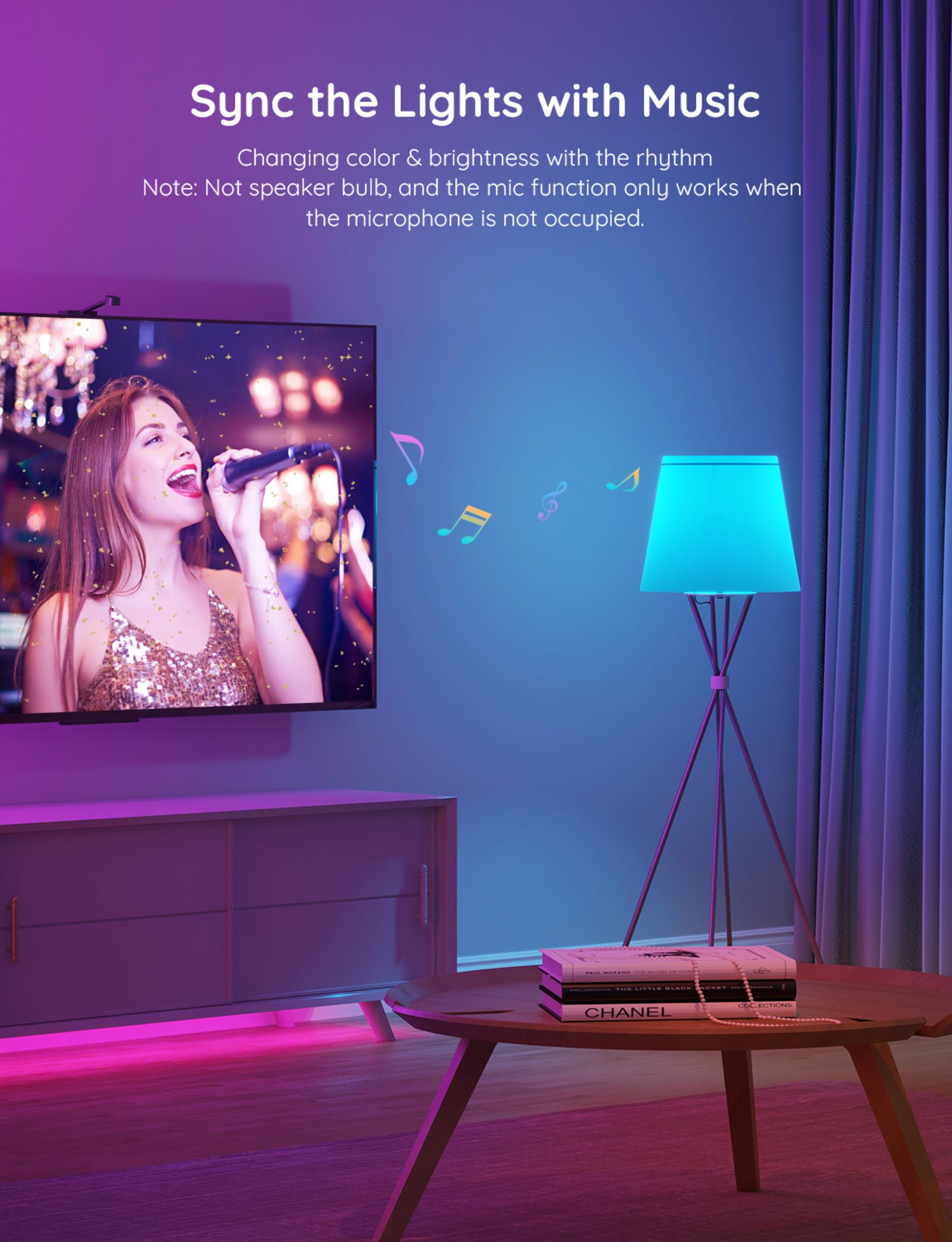 Eine Frau singt in ein Mikrofon vor einem Fernseher, daneben eine Lampe.