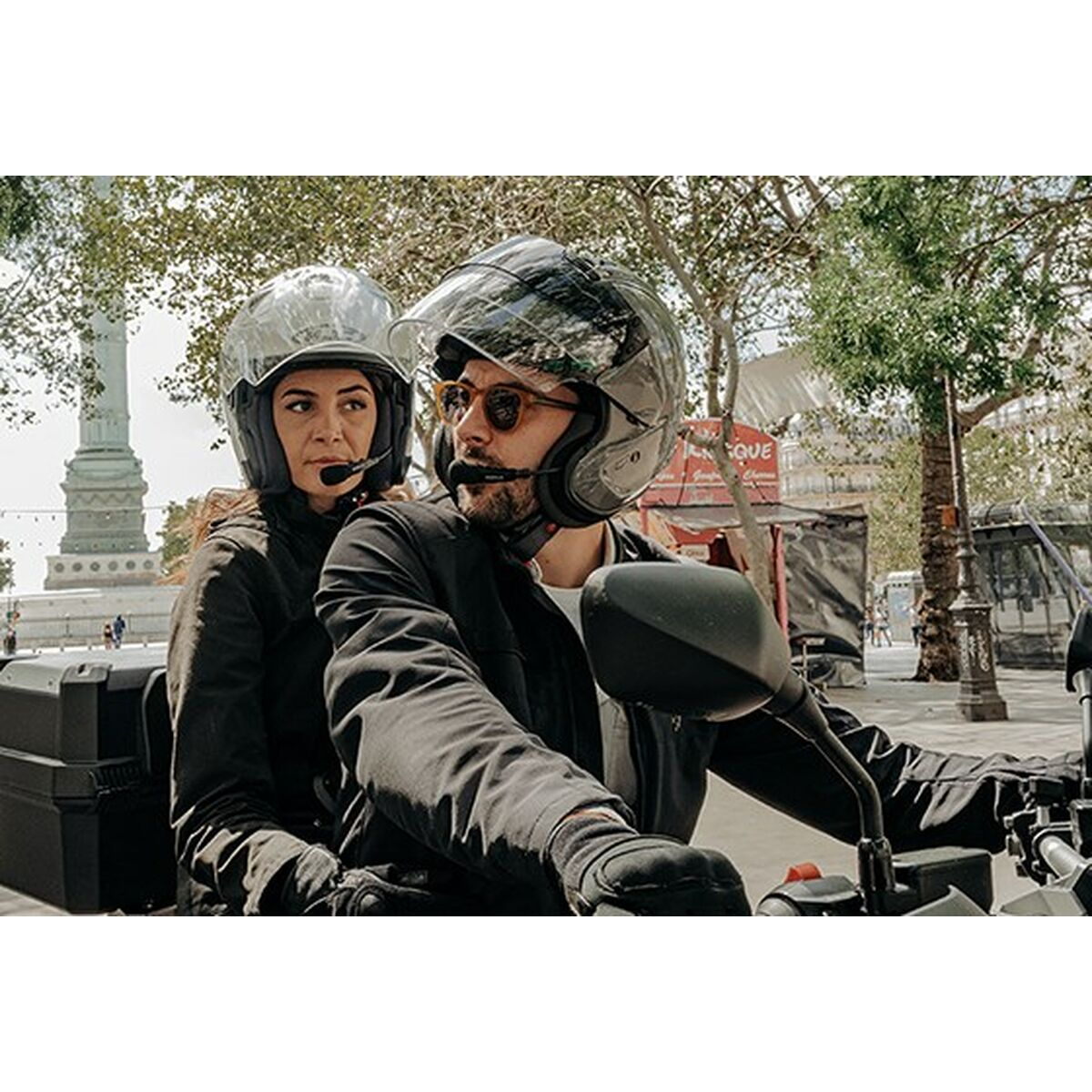 Mężczyzna i kobieta jadą motocyklem, oboje mają kaski i kurtki.