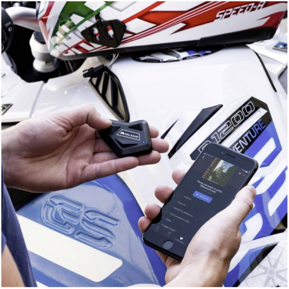 Dłonie trzymają urządzenie Midland i smartfon obok kasku i motocykla.