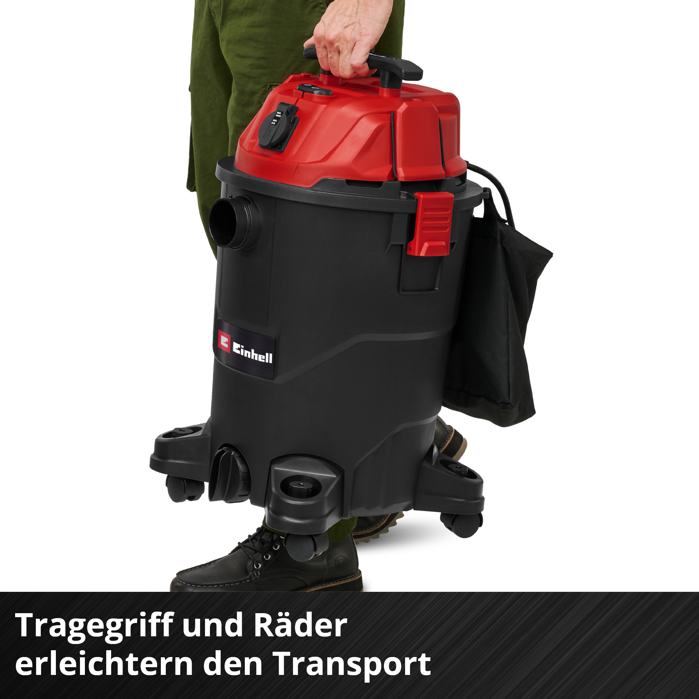 Person trägt schwarzen Einhell Nass-/Trockensauger mit rotem Deckel und Rädern.