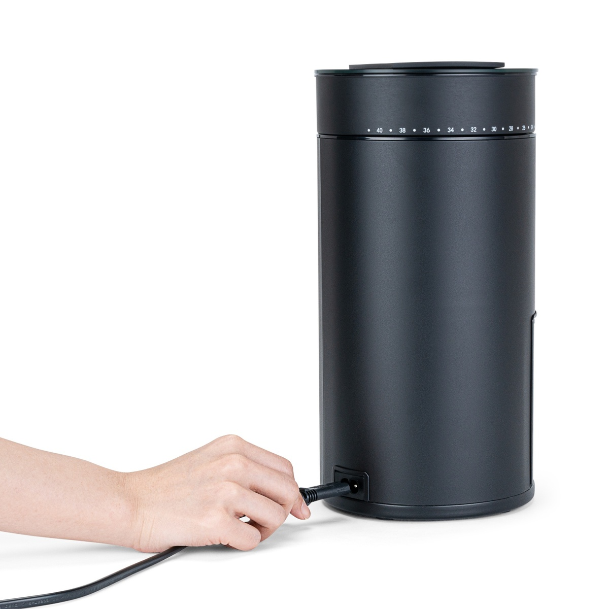 Eine Hand steckt ein schwarzes Kabel in einen schwarzen zylindrischen Behälter.