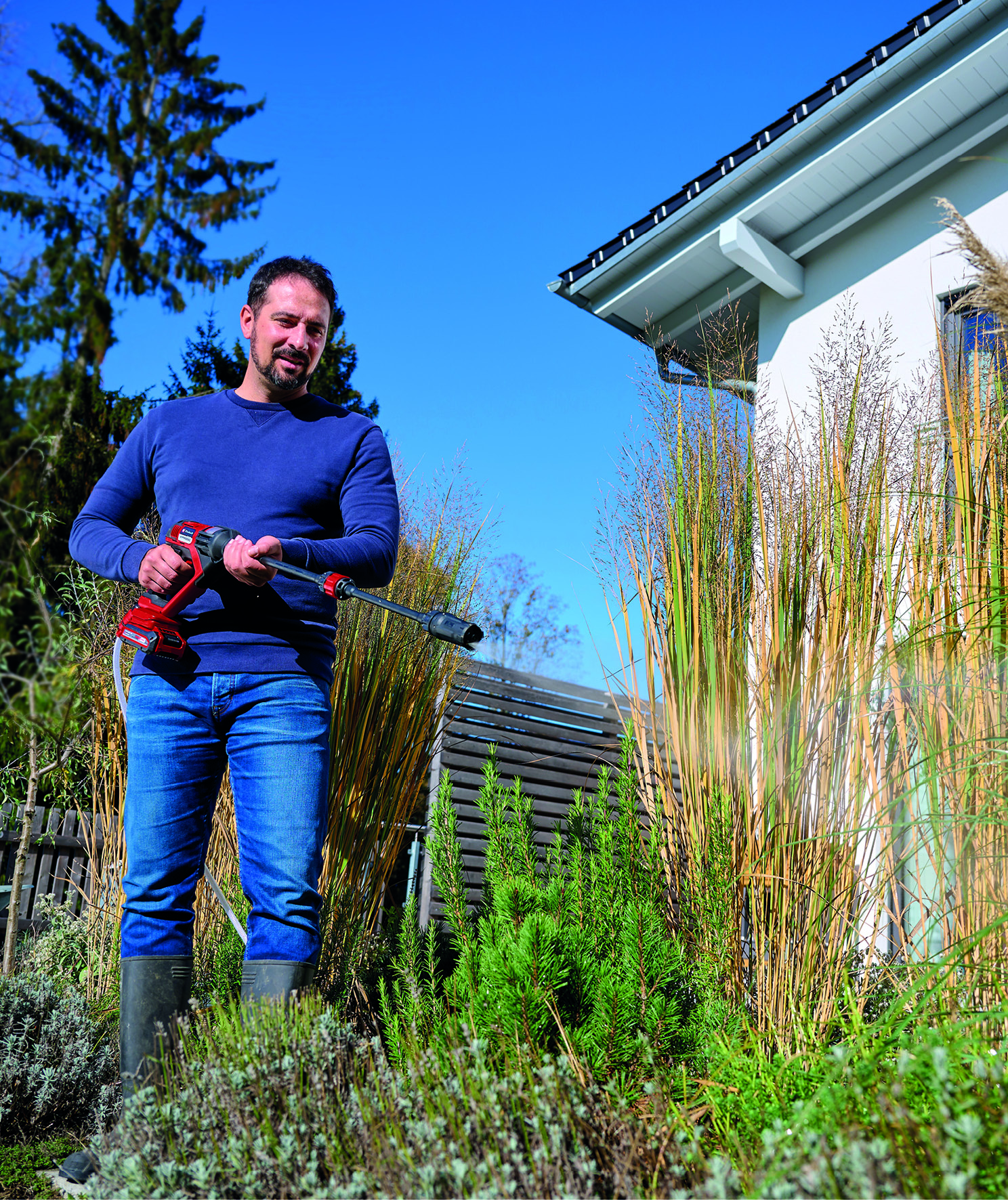 Homme avec nettoyeur haute pression dans jardin près d'une maison.