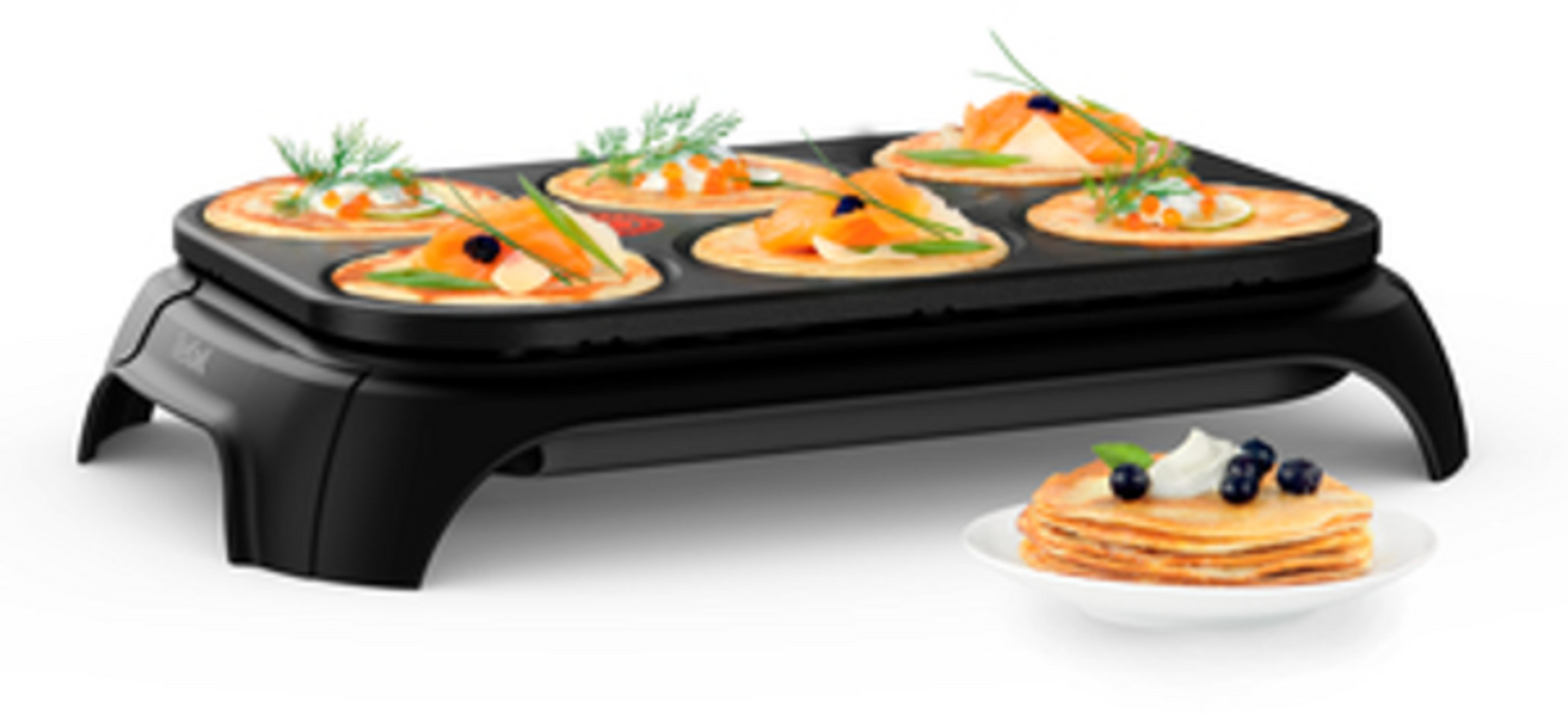 Elektryczna patelnia do naleśników z sześcioma napełnionymi naleśnikami i stosem naleśników obok.