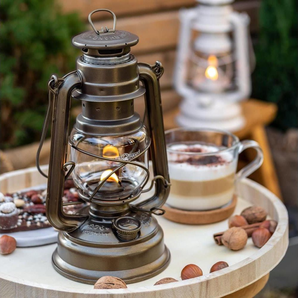 Eine antike Laterne mit brennender Flamme, daneben ein Kaffee und Nüsse.