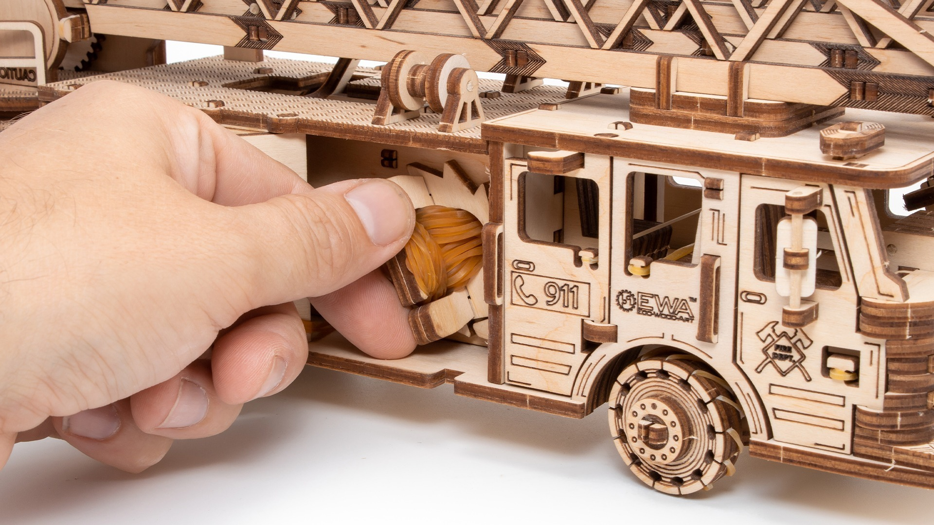 Eine Hand setzt Gummibänder in ein Holzmodell eines Feuerwehrautos ein.