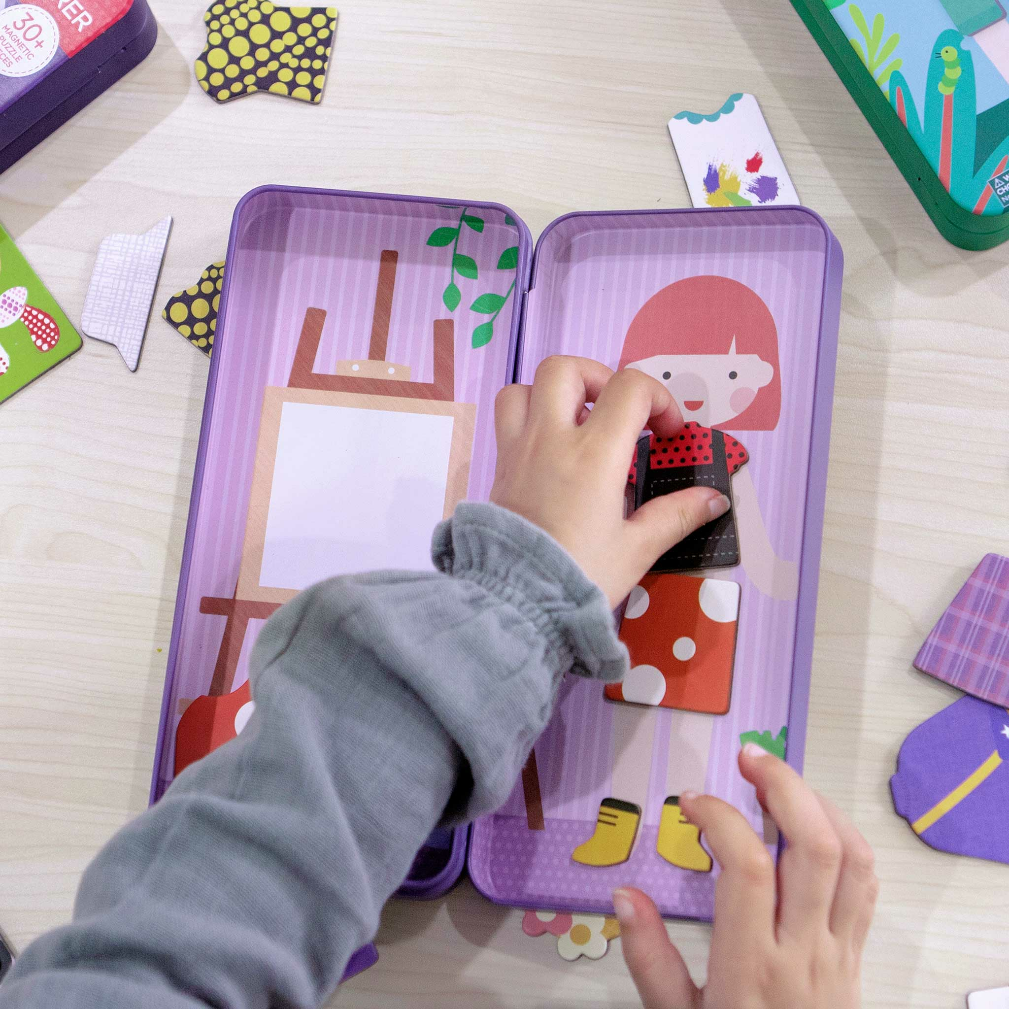 Ein Kind kleidet eine Papierpuppe mit magnetischen Teilen an einem aufklappbaren Spielzeug an.