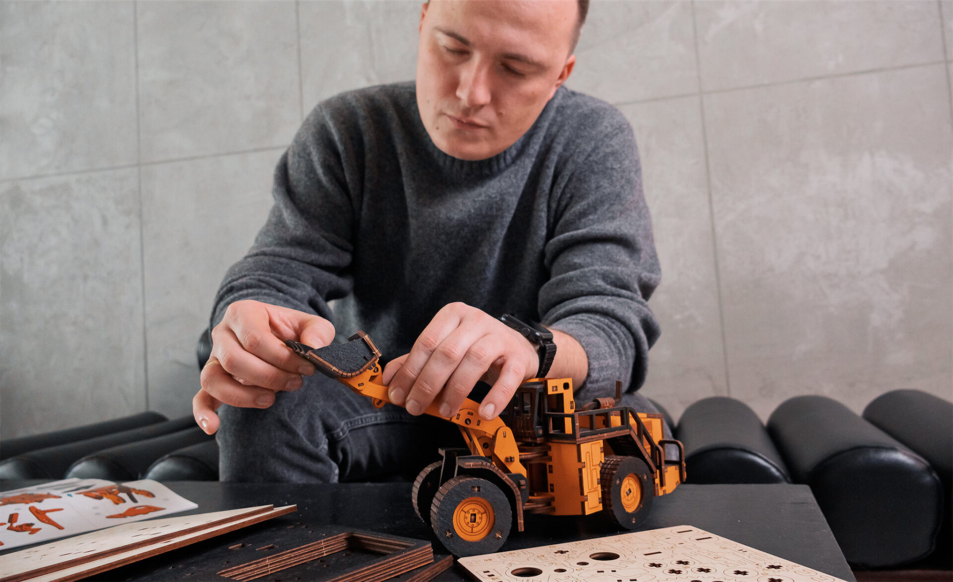 Ein Mann baut ein orangefarbenes Holzmodell eines Radladers an einem Tisch.