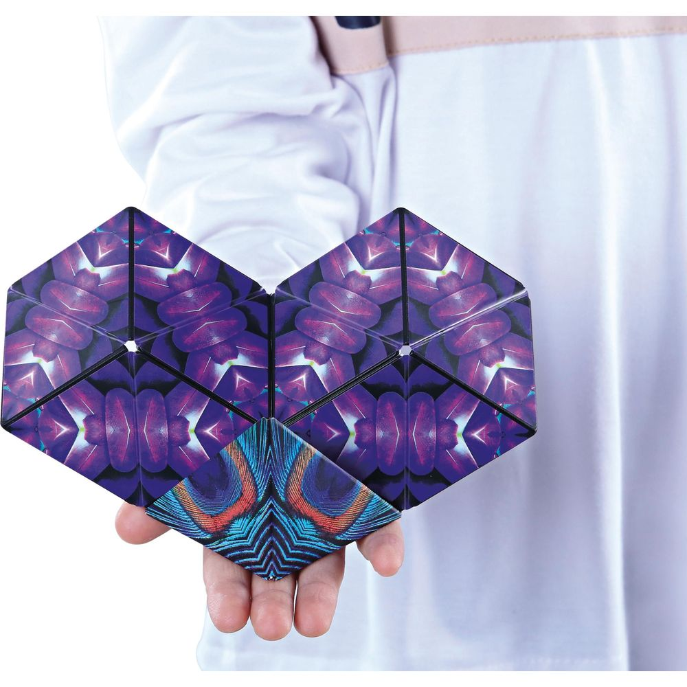 Una mano tiene un puzzle di pezzi esagonali con motivi di piume viola e blu.