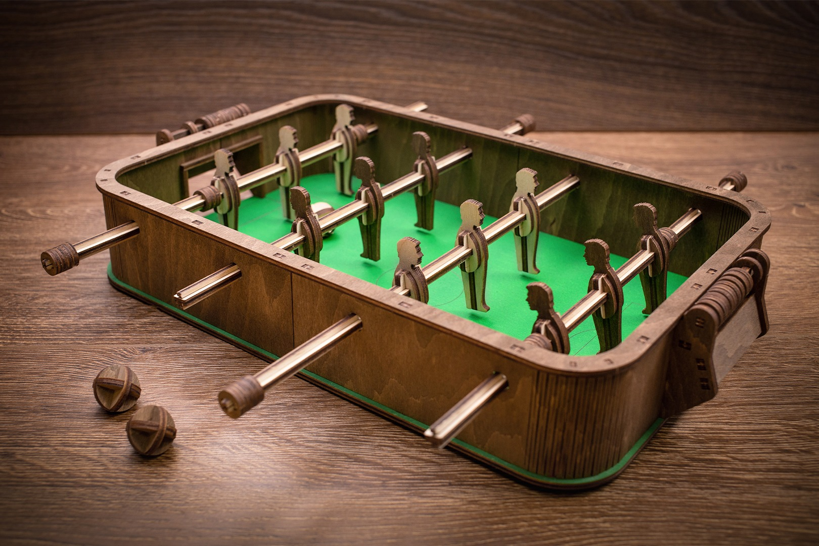 Ein hölzerner Tischfußballkasten mit grüner Spielfläche und Figuren.