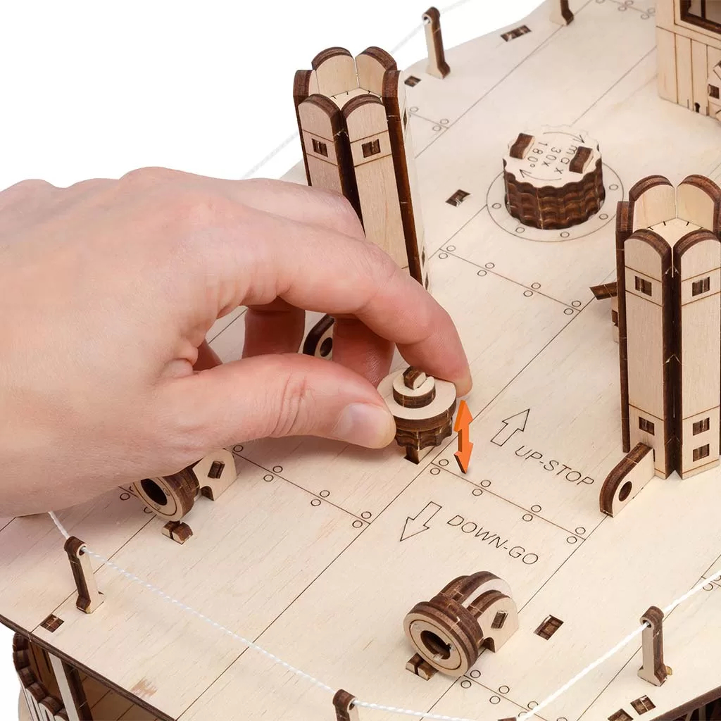 Eine Hand setzt ein kleines Holzteil in ein Modell ein. Zwei orangefarbene Pfeile zeigen Auf und Ab.